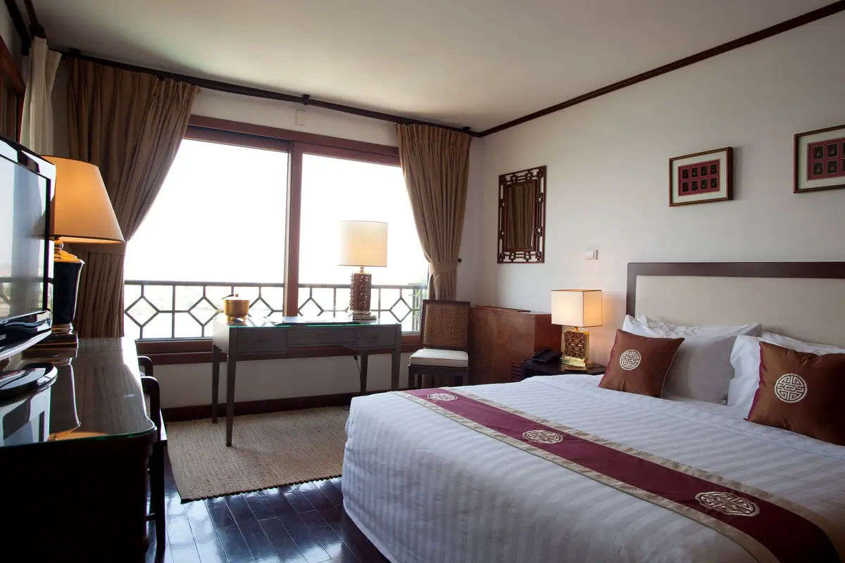 Bedroom with a double bed, red runner, bedside lamps and a window onto a balcony