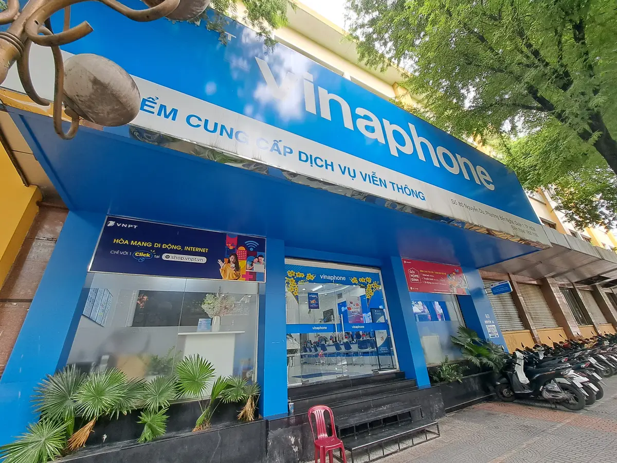 Blue VinaPhone shopfront on a tree-lined street with the logo above a glass door and steps at the entrance