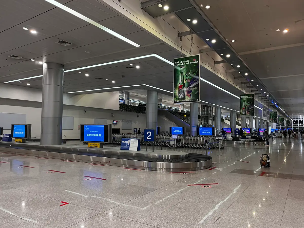 Baggage claim hall at Tan Son Nhat International Airport with carousels, overhead screens and signs
