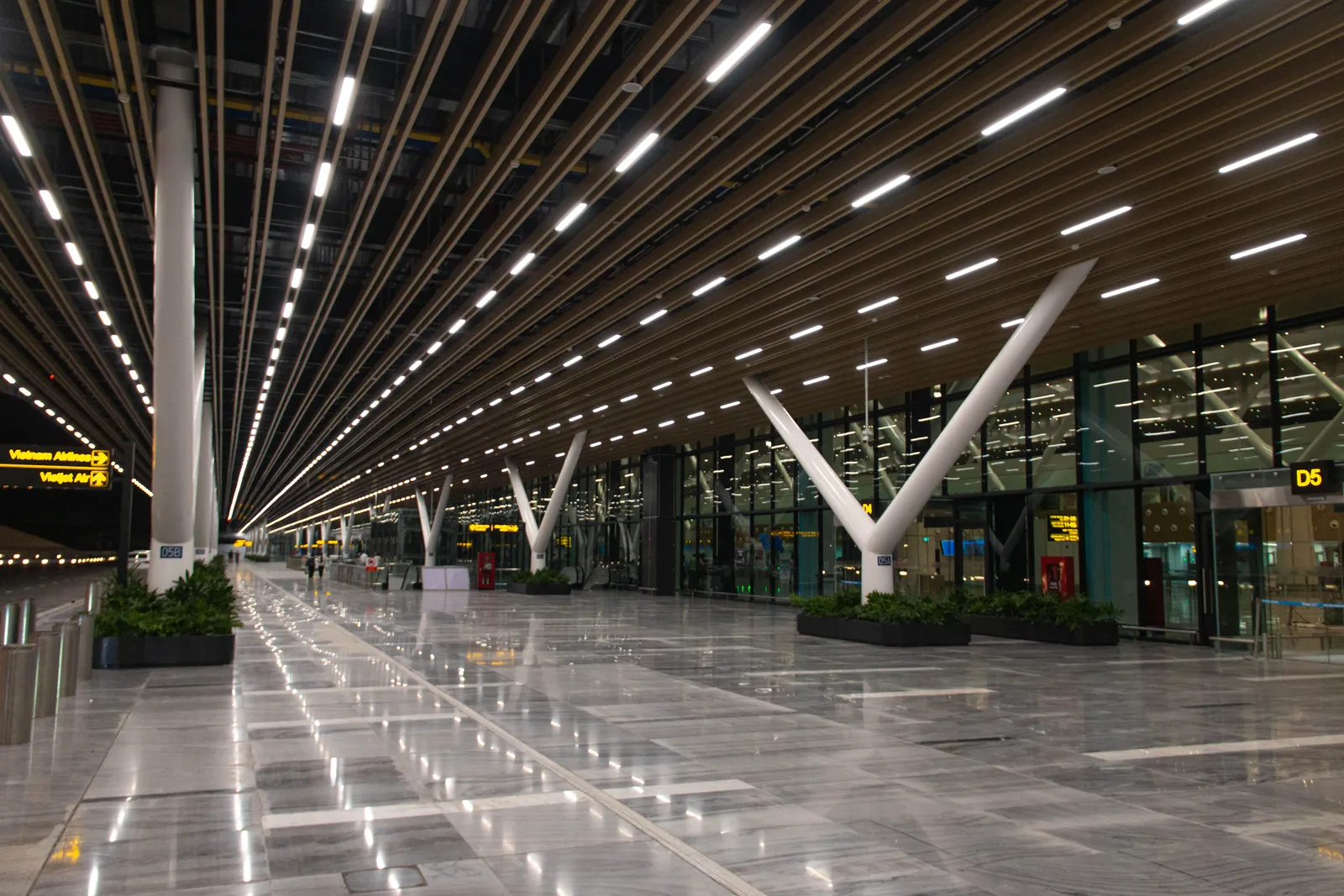 Long empty concourse with a slatted wooden ceiling, white Y-shaped columns and glass walls