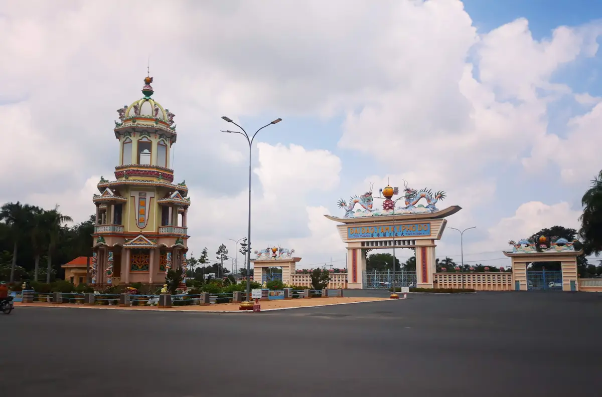 Tall tower beside a wide empty road and a decorated gate under a cloudy sky
