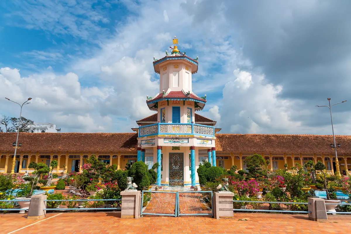 Small white and blue tower at the end of a garden path in front of a long tiled-roof building