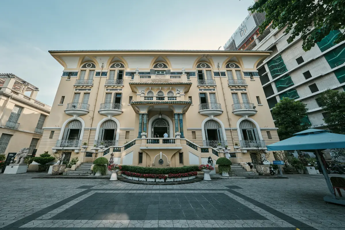 Cream and yellow colonial villa with arched windows and balconies behind a paved forecourt