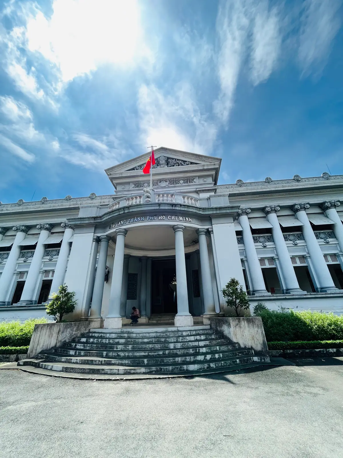 White neoclassical museum building with tall columns, a front staircase and a red flag