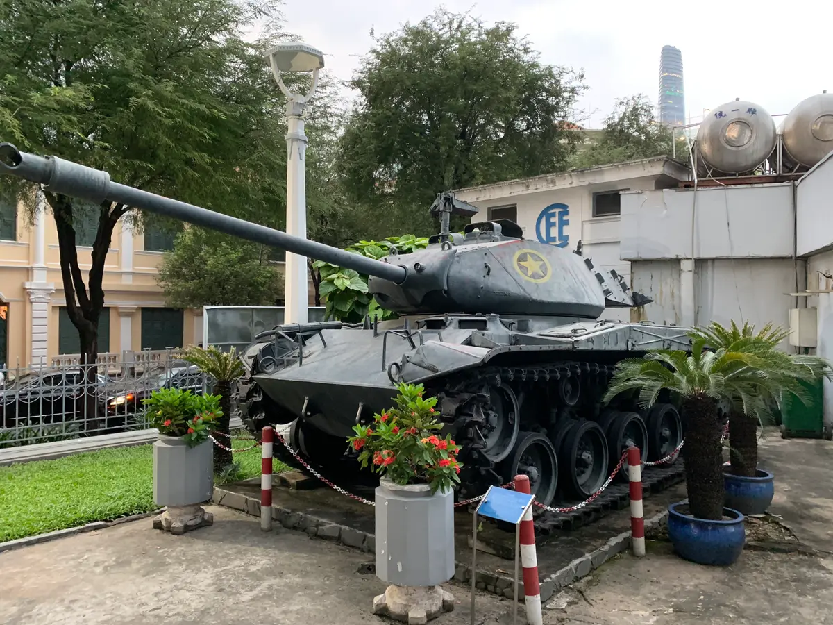 Green tracked tank with a long gun barrel on display beside palm plants