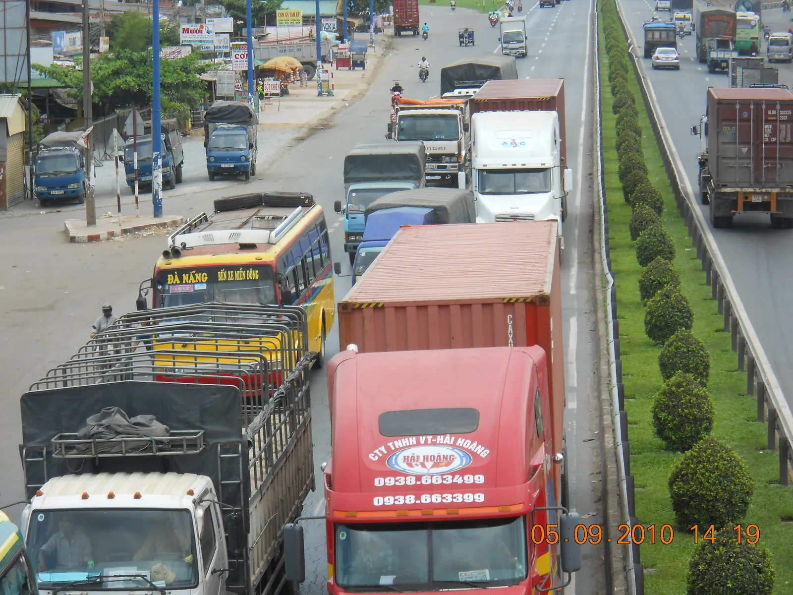 Trucks and buses in heavy traffic on a wide highway with a planted median