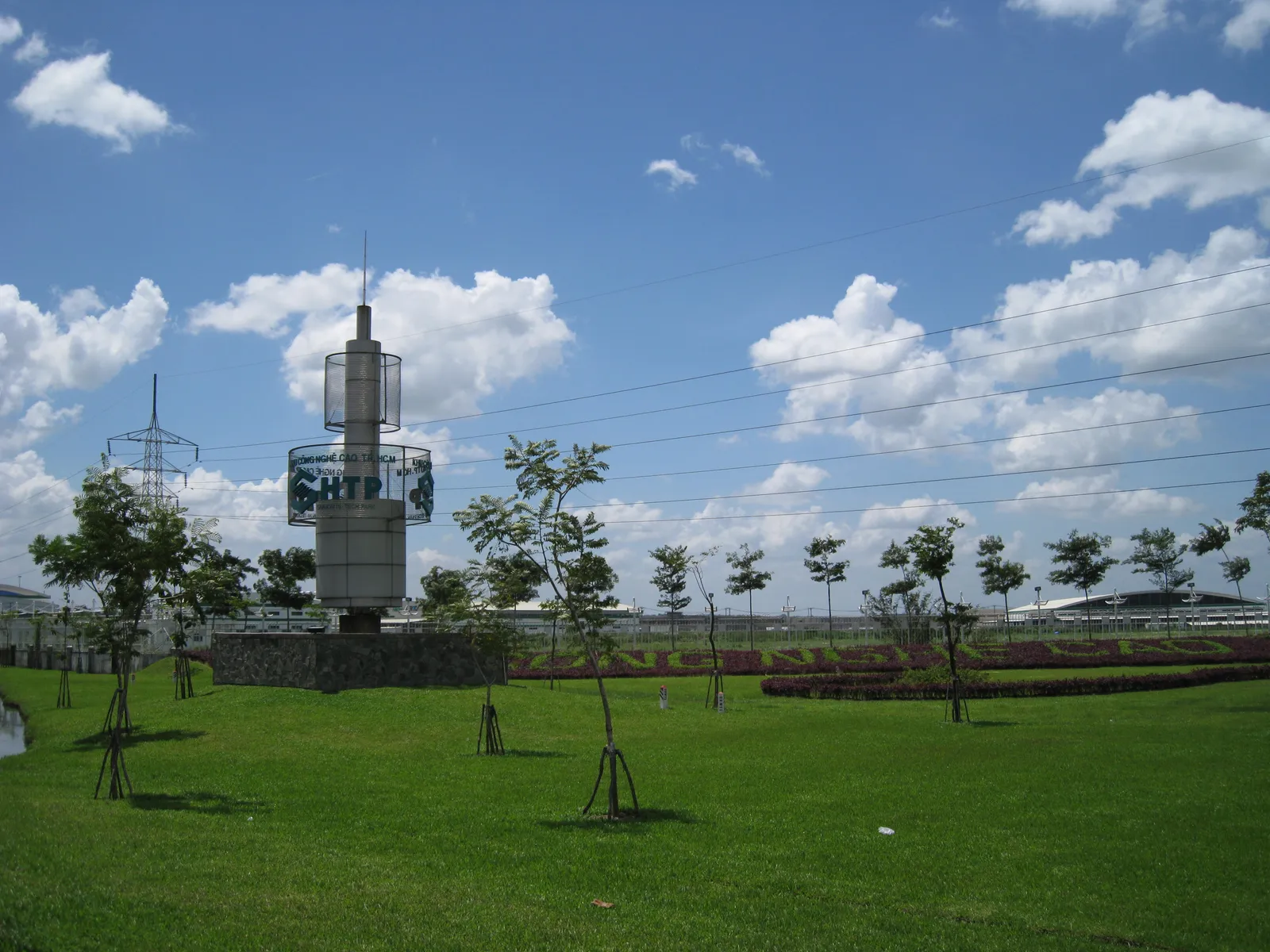Grass lawn and a tall sign tower at the edge of a business park under blue sky
