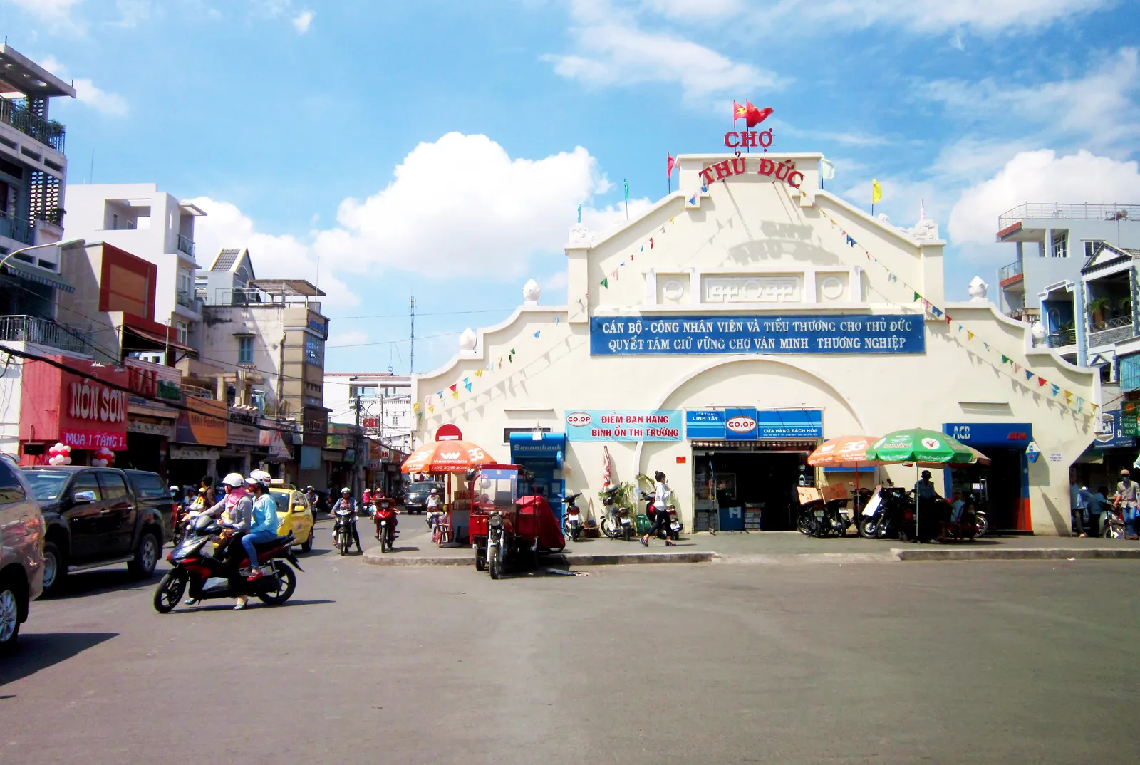 White market building with a blue sign at a junction, motorbikes passing