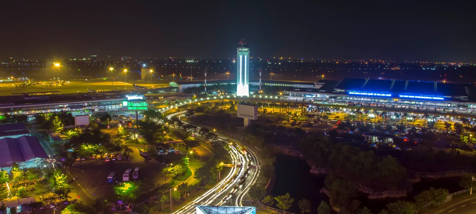 Night view of an airport terminal and control tower beside a lit access road and car park