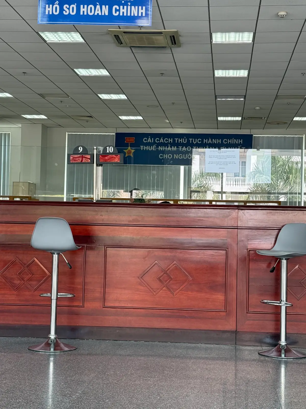 Reception counter of polished wood with grey bar stools and numbered windows behind it.