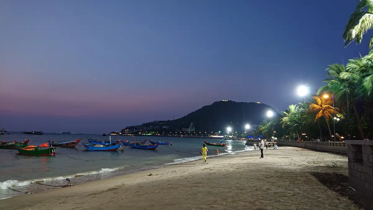 Lit promenade and fishing boats on a sandy beach at dusk