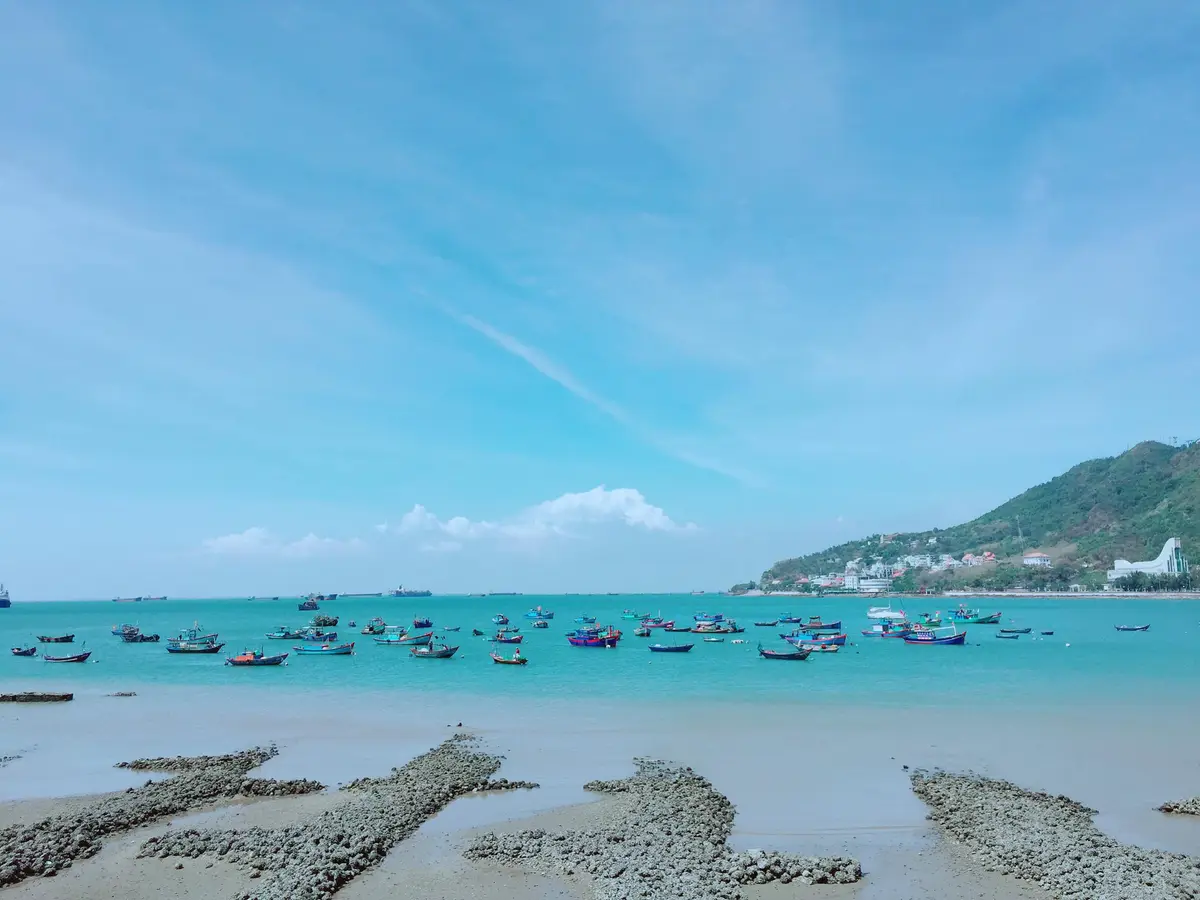 Turquoise shallow water with rocky ridges and small boats near a green headland