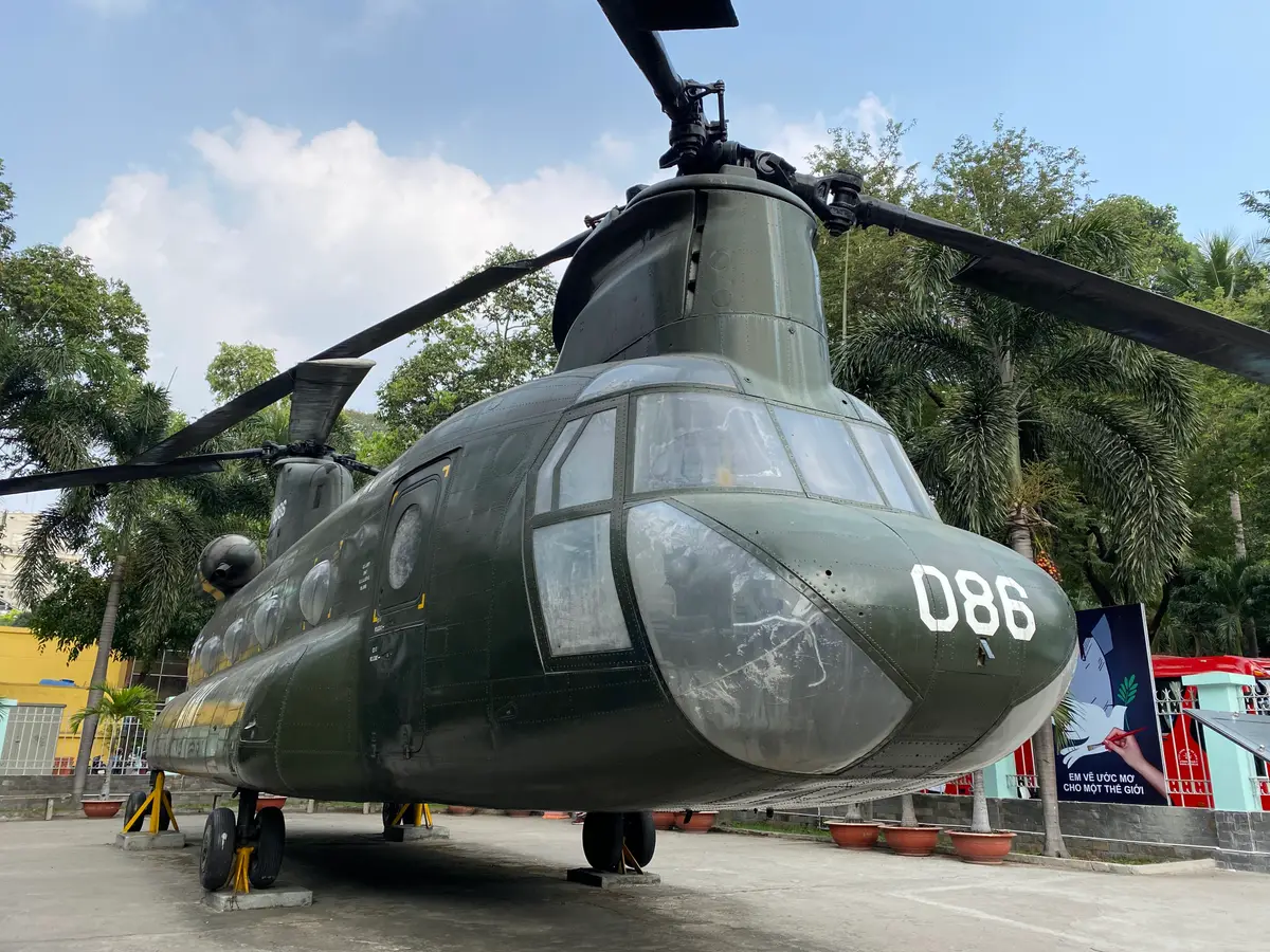 Large olive green twin-rotor transport helicopter on display under palm trees