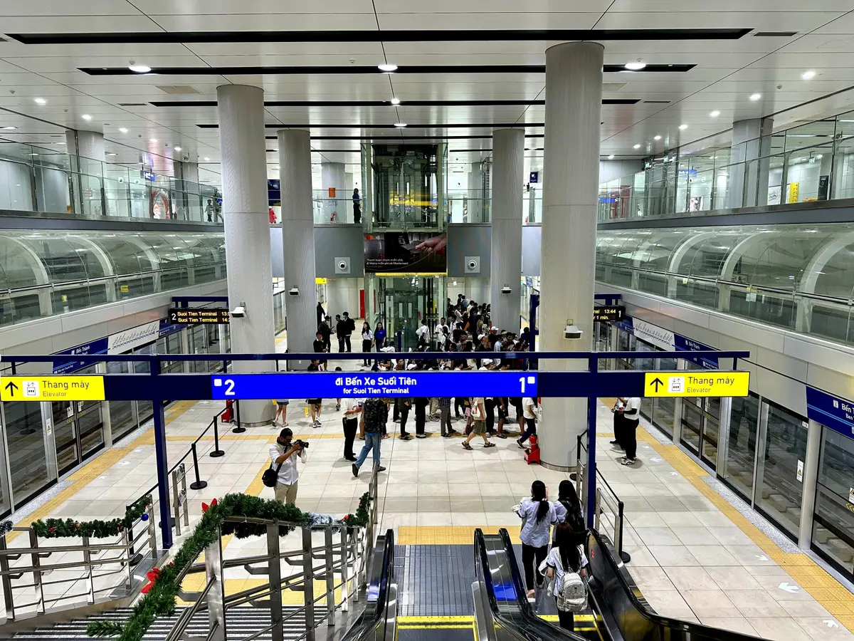 Underground metro hall with escalators, a blue direction sign and passengers on the platform level