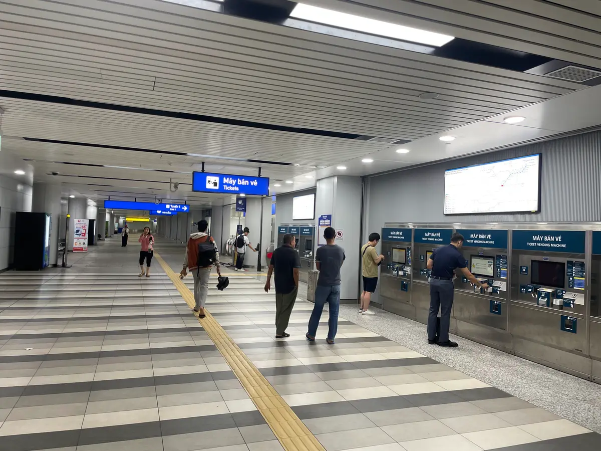 Metro station concourse with a row of ticket machines and passengers standing in front of them